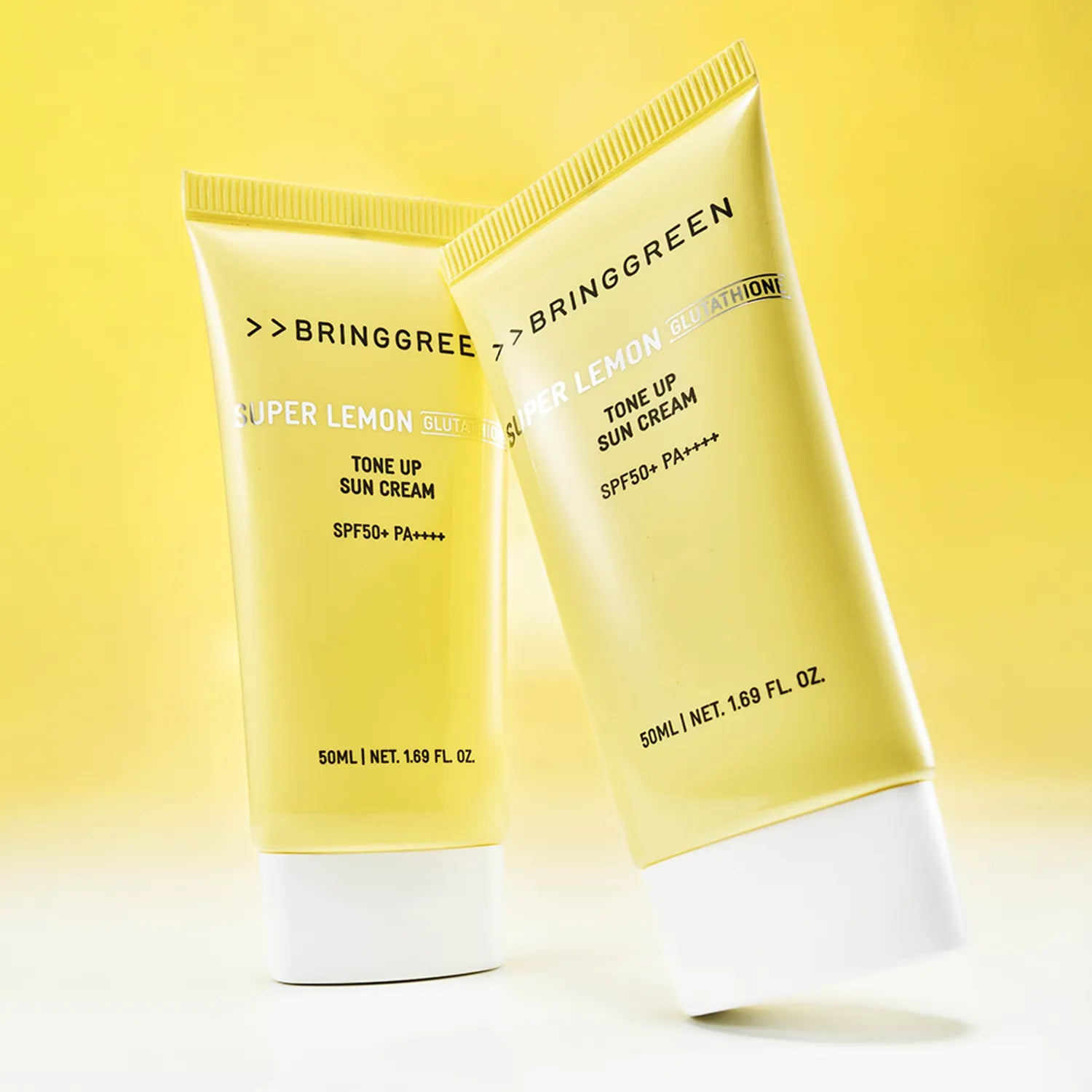 BRINGGREEN Super Lemon Glutathione Tone-Up Sun Cream 50ml+50ml SPF 50+ / PA++++ en tubes sur fond jaune ensoleillé