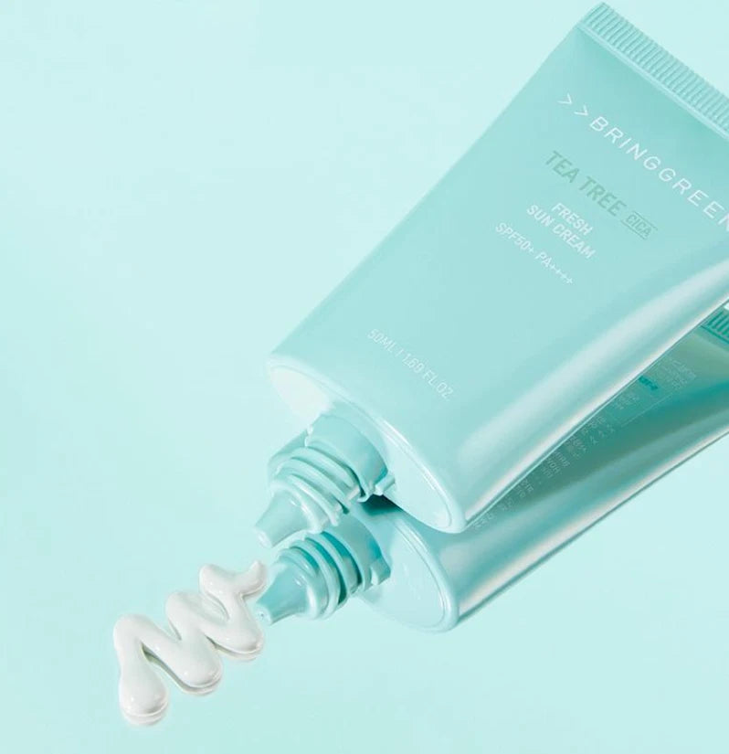 BRINGGREEN Teatree Cica Fresh Sun Cream 50ml de la marque sur fond bleu pastel, tube et gouttes crème visibles.