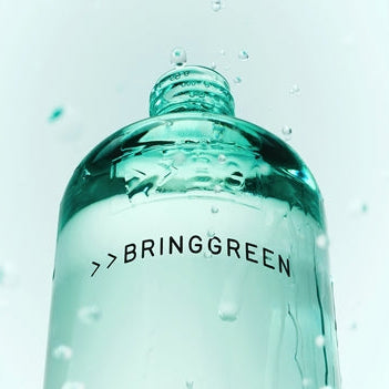 Décris l'image en français: BRINGGREEN Teatree Cica Soothing Toner 250ml/500ml de BRINGGREEN, bouteille verte avec gouttes d'eau.