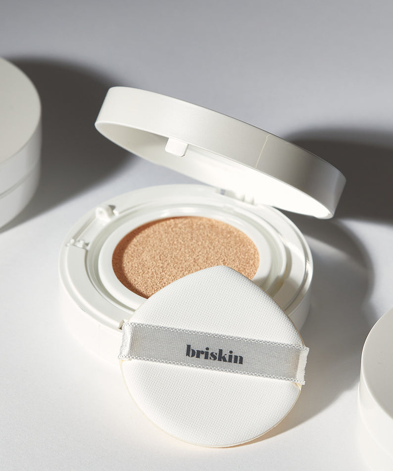 Coussin maquillage BRISKIN Exo-Glow Secondskin Cushion 15g en boîtier blanc ouvert, avec applicateur en éponge blanc.