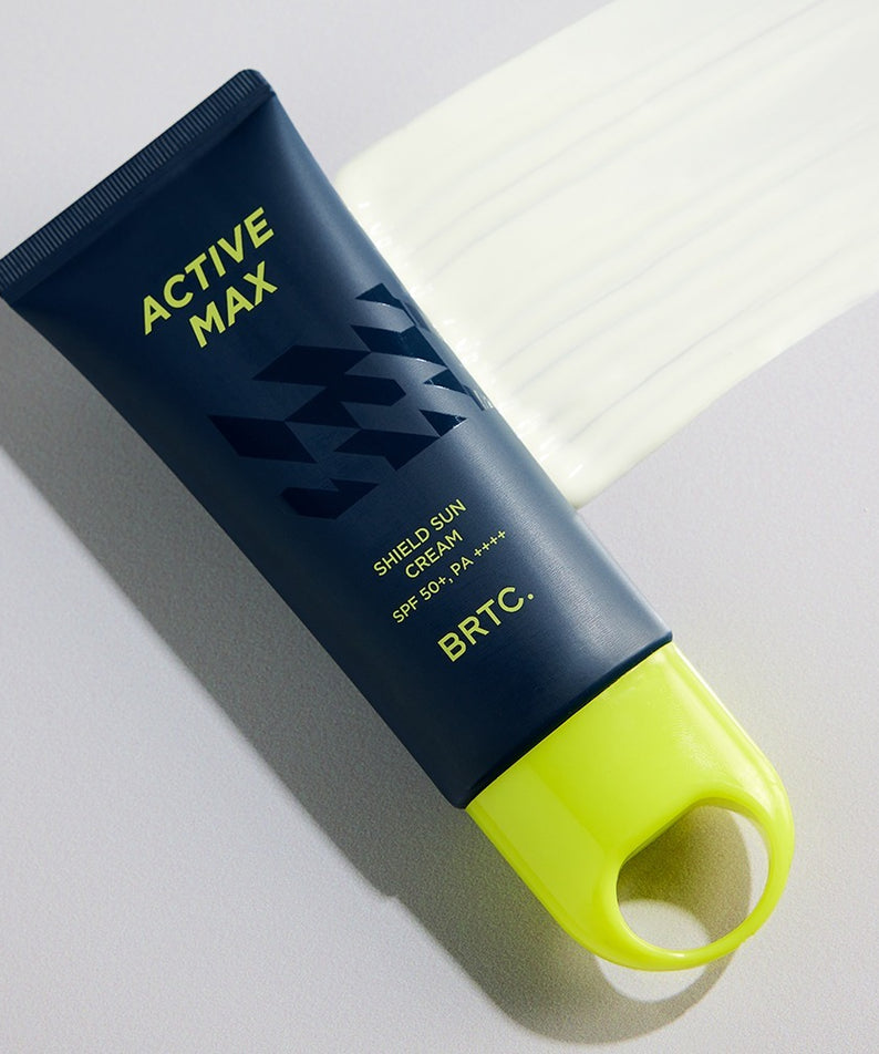 Décris l'image en français : BRTC Homme Active Max Sheild Sunscreen 50ml, tube bleu, contexte soins visage au soleil.