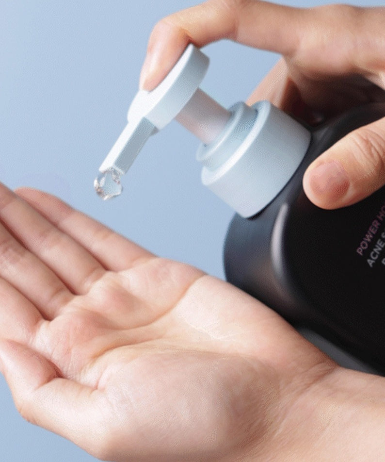 Main utilisant BRTC Power Homme Acne Solution Body Wash 500ml de BRTC sur peau, flacon-pompe sur fond bleu.