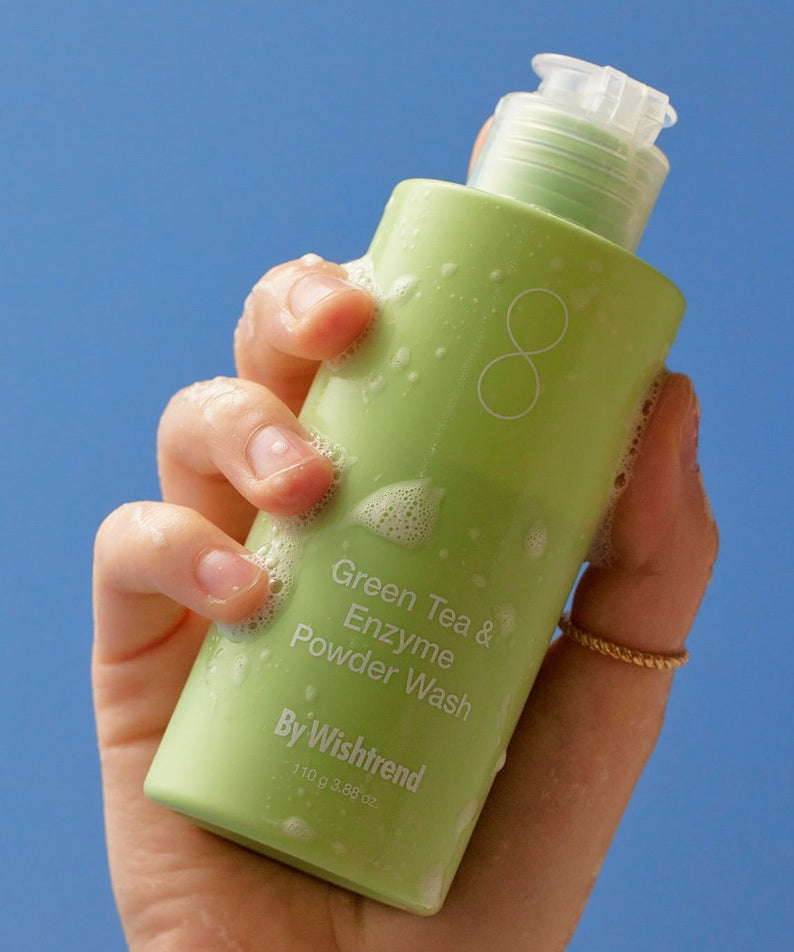 BY WISHTREND Green Tea & Enzyme Powder Wash 110g : flacon vert en main, fond bleu, vue produit.