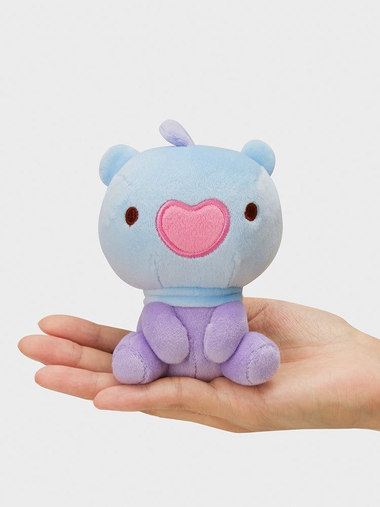 Main tenant BT21 MANG minini LYING DOLL, peluche officielle BT21 représentant MANG poney danseur masqué, fond clair.