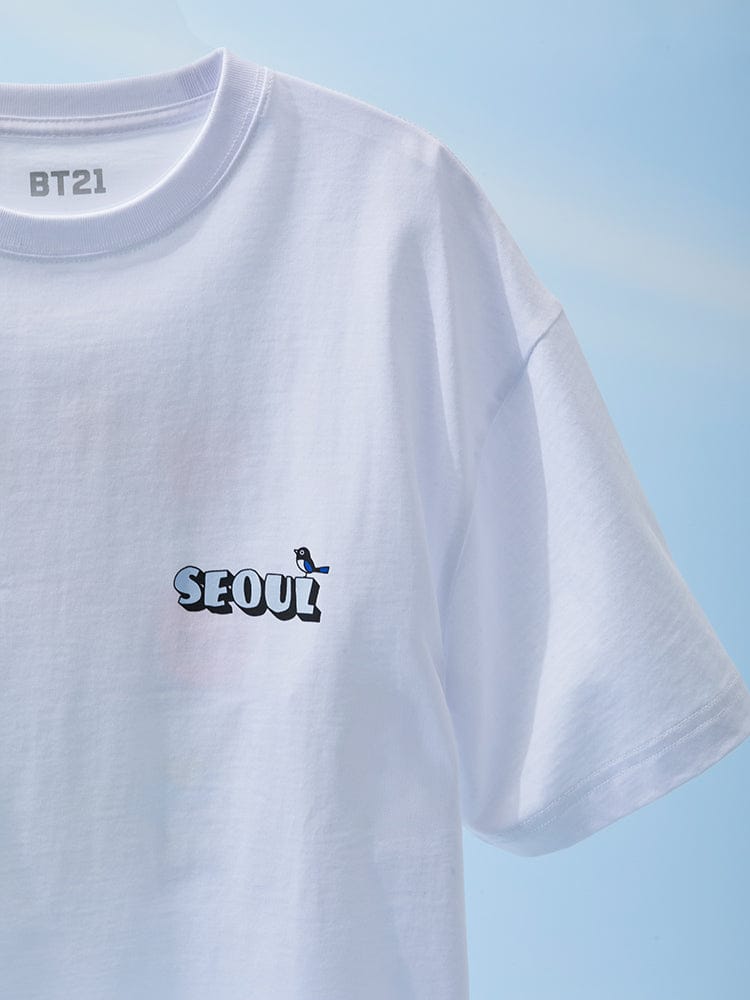BT21 SHORT SLEEVE T-SHIRT WHITE WORLD VOYAGE : t-shirt blanc LINE FRIENDS, personnage SEOUl, vue gros plan devant ciel bleu.