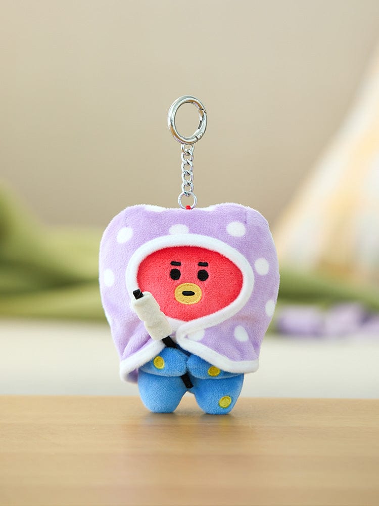 BT21 TATA DOLL KEYRING CAMPFIRE, porte-clés TATA LINE FRIENDS avec figurine violette, sur table près d’un décor flou.