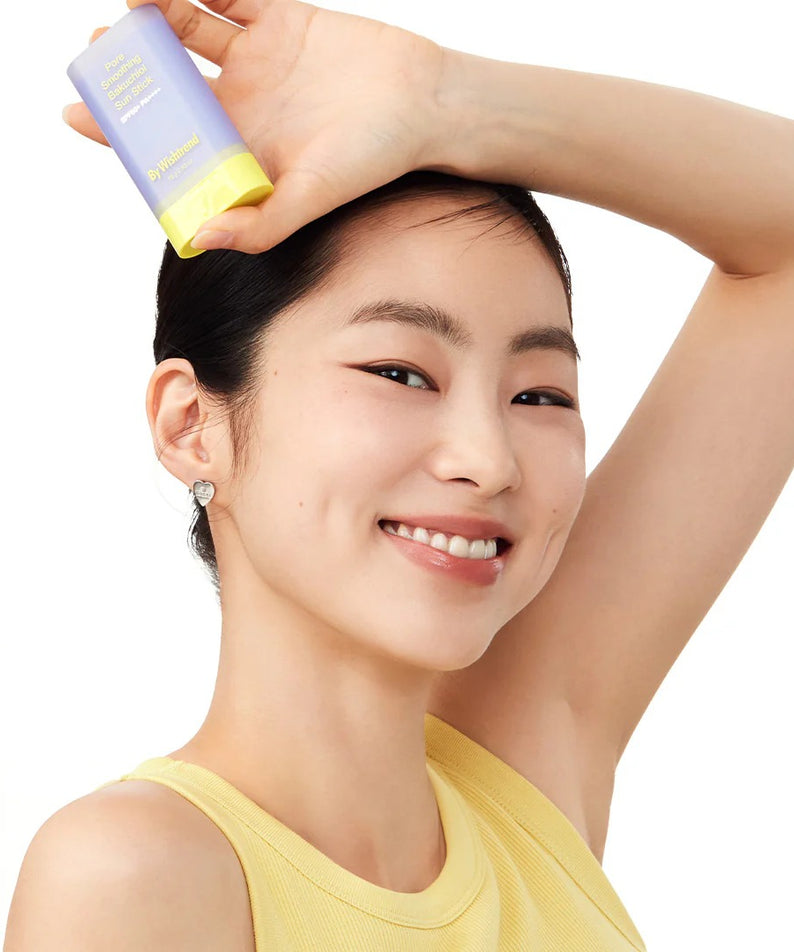 Femme souriante tenant le BY WISHTREND Pore Smoothing Bakuchoil Sun Stick 18g, produit de soin solaire.