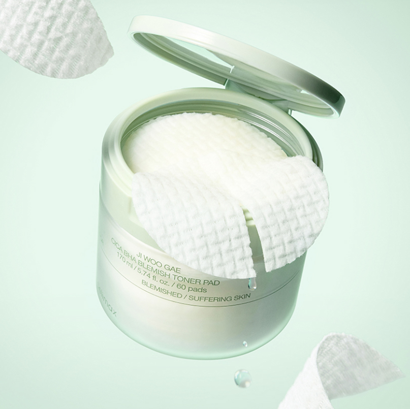 Décris l'image en français : CELIMAX Ji Woo Gae Cica BHA Blemish Toner Pad 60 pads, boîte ouverte avec pads, fond pastel.