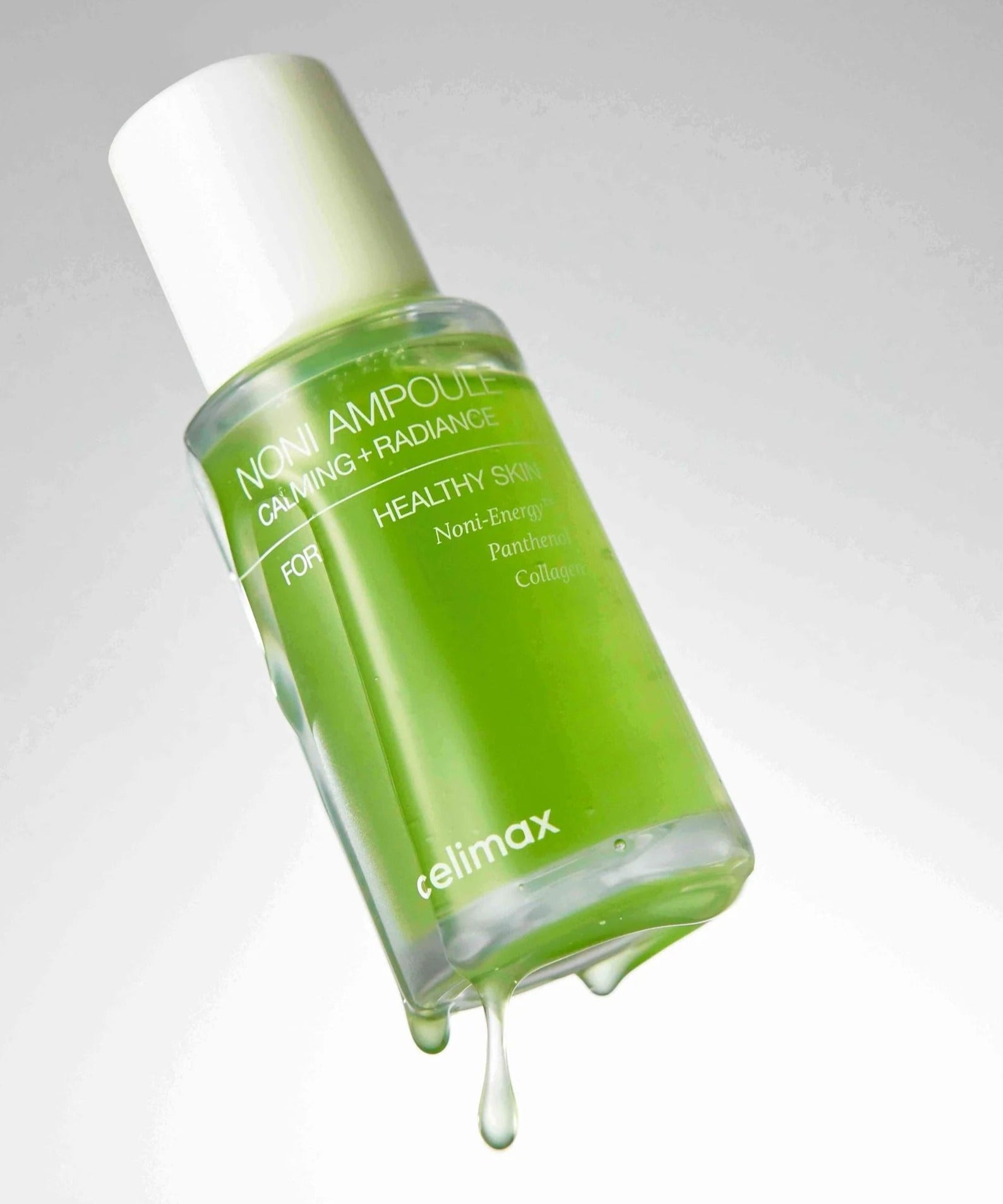 CELIMAX Noni Ampoule Calming+Radiance 100ml : flacon vert avec gouttes, produit beauté apaisant sur fond clair.