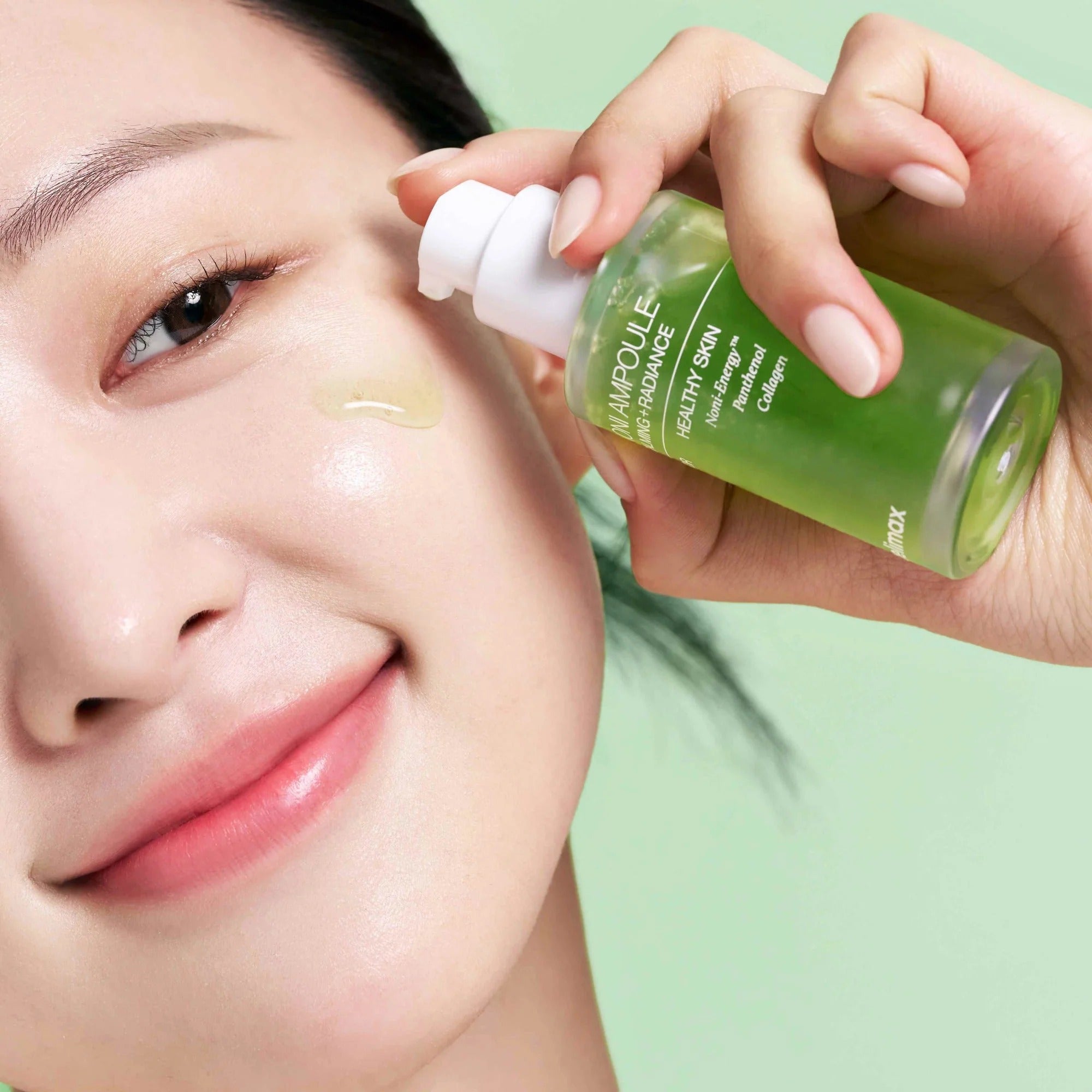 CELIMAX Noni Ampoule Calming+Radiance 100ml : femme applique une ampoule apaisante sur le visage, bouteille verte, contexte beauté.