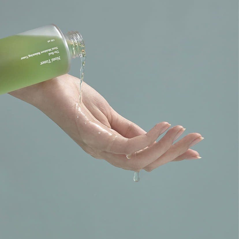 CELIMAX The Real Noni Moisture Balancing Toner 320ml : la main reçoit le toner sur une peau, contexte visuel soin beauté