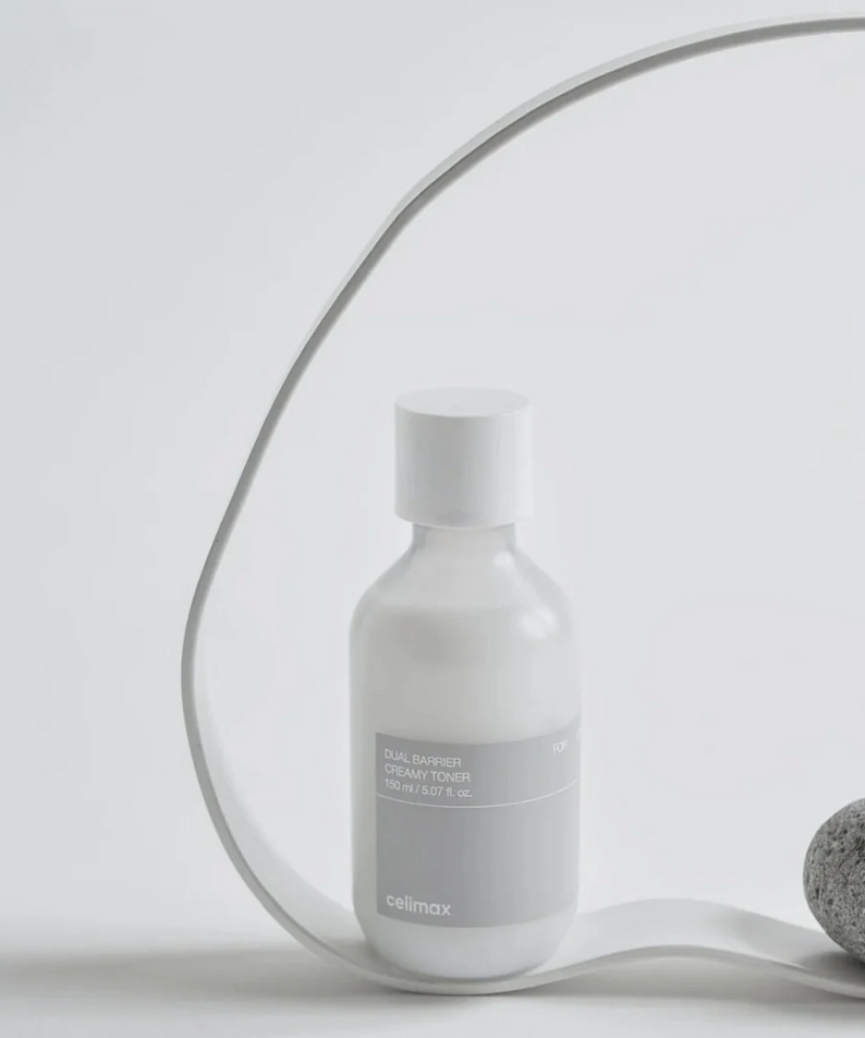 Bouteille de CELIMAX Dual Barrier Creamy Toner 150ml sur fond minimaliste avec pierre décorative grise. Produit de soin hydratant.