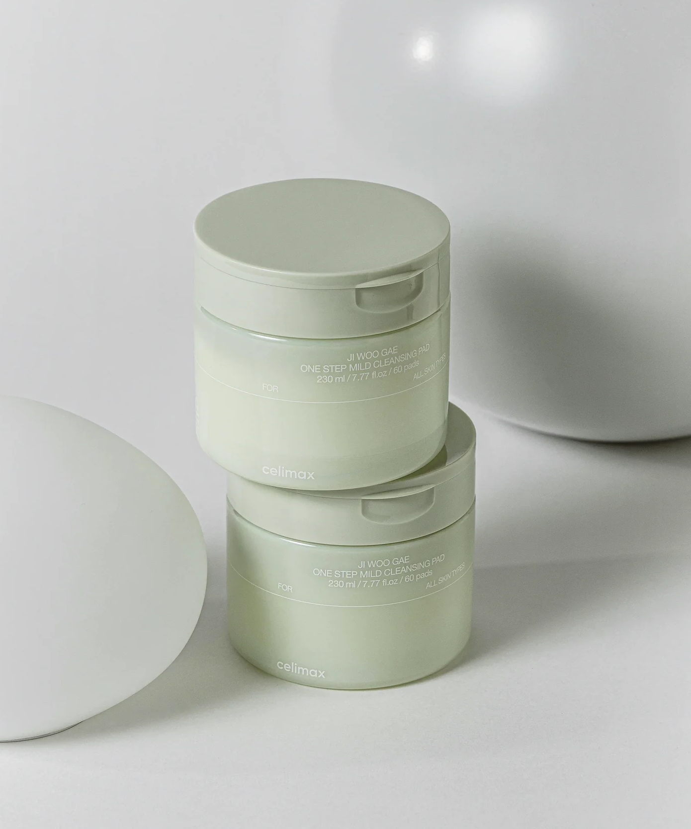 Deux pots de CELIMAX Ji Woo Gae One Step Mild Cleansing Pad 60 pads sur une surface beige élégante.