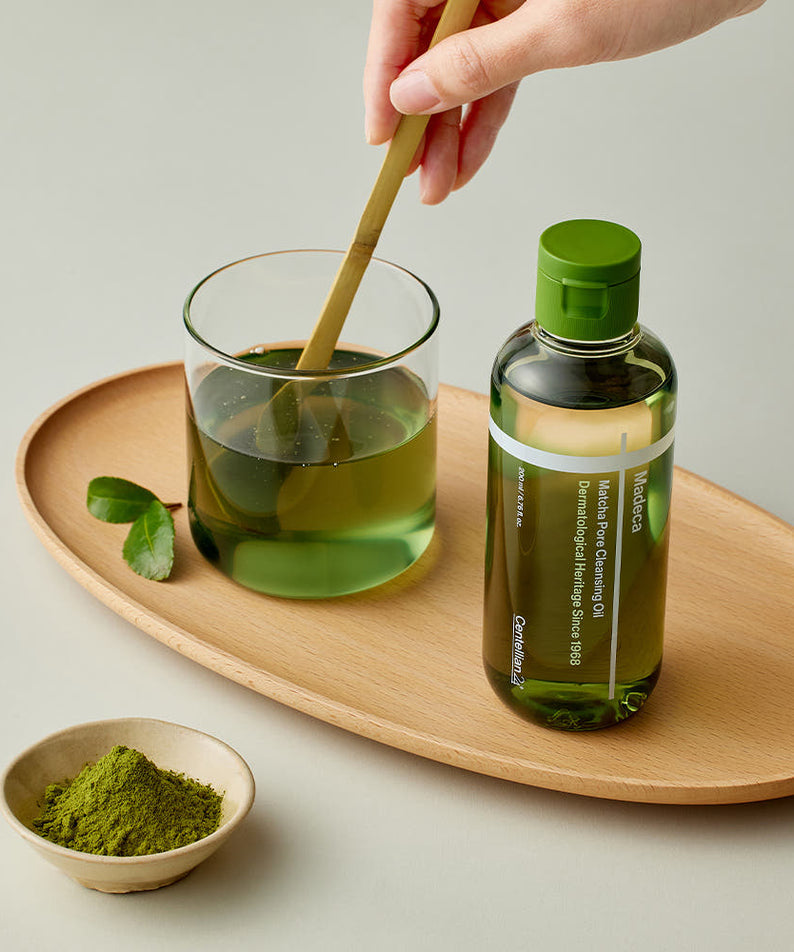 Main verse CENTELLIAN 24 Madeca Matcha Cleansing Oil 200ml, marque sur flacon vert, poudre matcha sur plateau bois.
