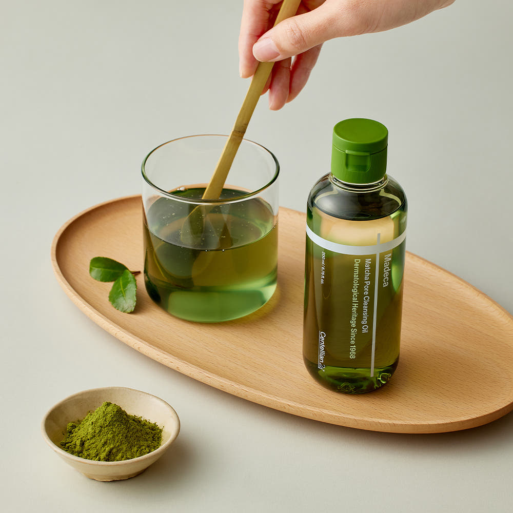 Main verse CENTELLIAN 24 Madeca Matcha Cleansing Oil 200ml, marque sur flacon vert, poudre matcha sur plateau bois.