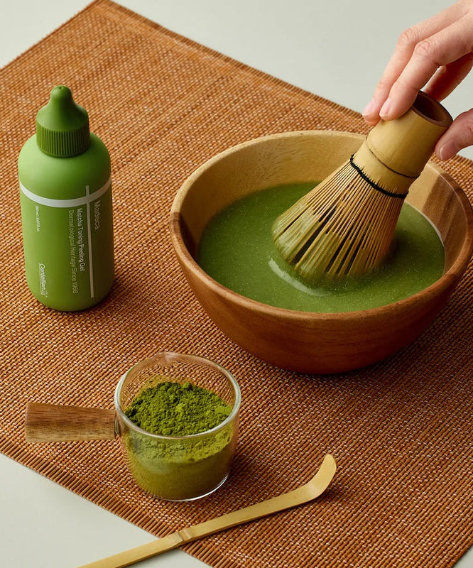 Préparation de thé vert matcha avec CENTELLIAN 24 Madeca Matcha Toning Peeling Gel 150ml sur une table en bois.