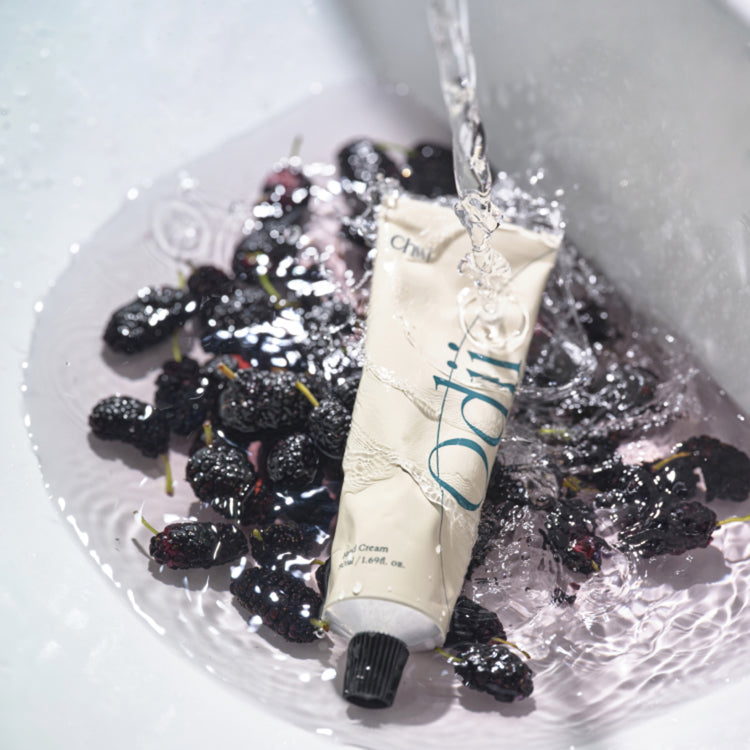 CHWI (CHI) Odii Hand Cream 50ml, tube avec eau sur fond de fruits noirs, visuel produit en studio.