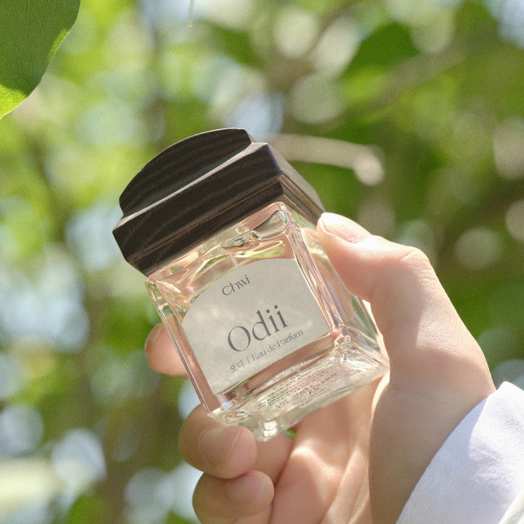 Main tenant CHWI (CHI) Odii Parfume 50ml, flacon transparent, arrière-plan jardin vert, marque CHWI