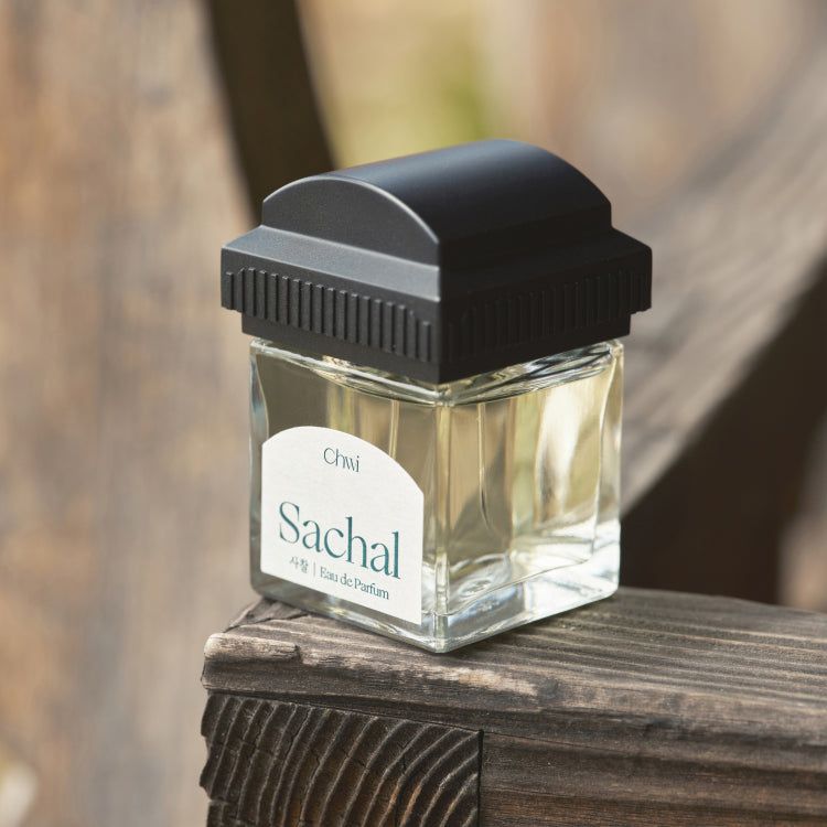 CHWI (CHI) Sachal Parfume 50ml, flacon sur table en bois, marque CHI, fond flou naturel, ambiance chaleureuse.