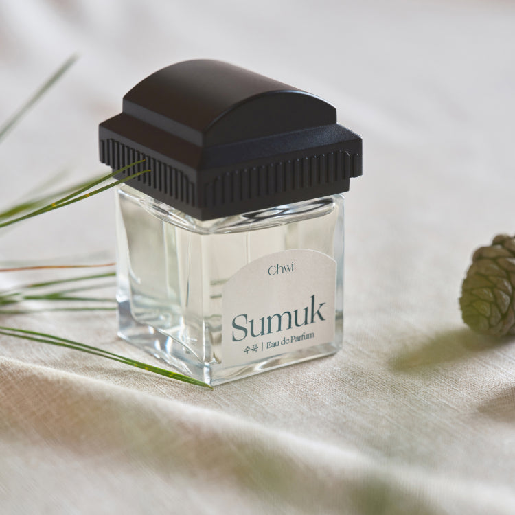 CHWI (CHI) Sumuk Parfume 50ml : flacon noir sur tissu beige, avec brins d’herbe et feuille, fond clair.