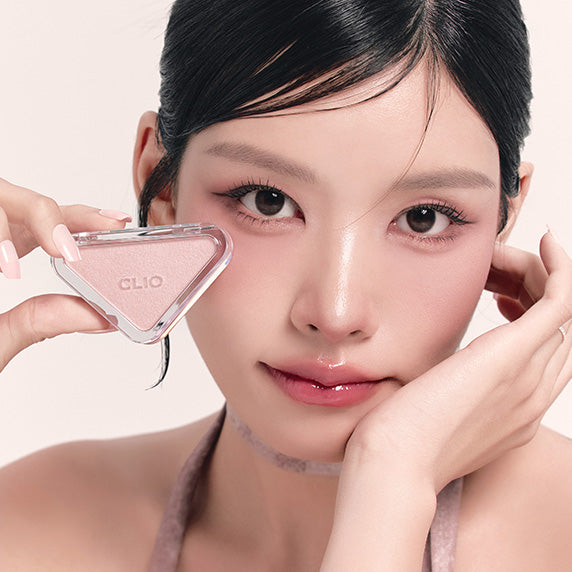 Photo maquillage : CLIO  Essential Blush Tab de la marque CLIO, visage de femme avec blush, outil dans les mains.