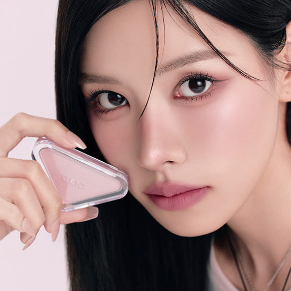 Portrait maquillage : CLIO  Essential Blush Tab, marque CLIO, sur visage aux joues rosées, main tenant le produit.