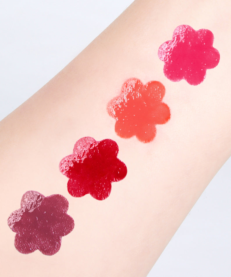 CORINGCO Pink Churrons Plumping Glossy Lip de la marque CORINGCO sur un avant-bras, swatches fleurs roses, fond clair.