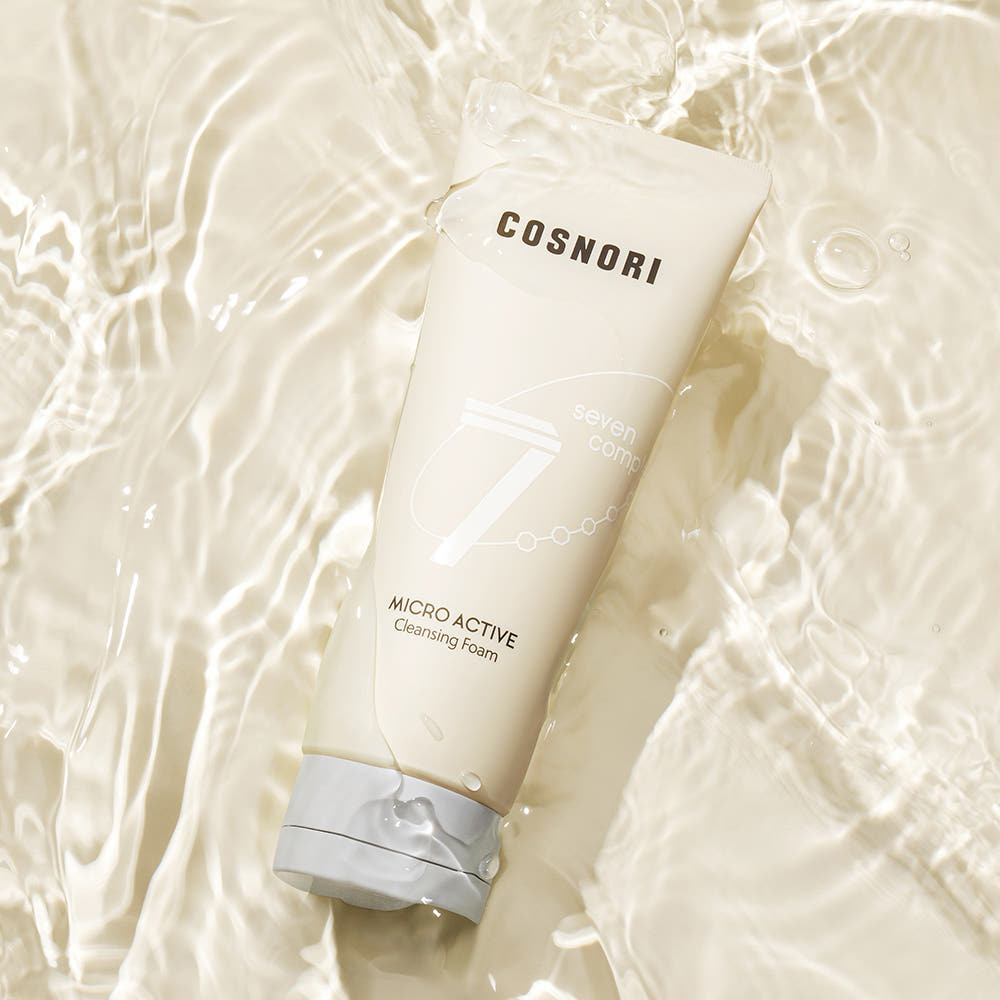 Décris l'image en français: COSNORI Micro Active Cleansing Foam 150ml 2ea, tube blanc sur fond crème avec bulles, contexte spa.