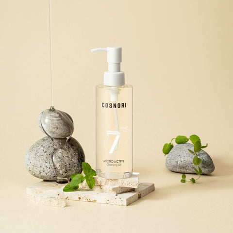 COSNORI Micro Active Cleansing Oil 200ml, bouteille blanche avec pompe, mise en scène minimaliste avec pierres et feuilles, beige.