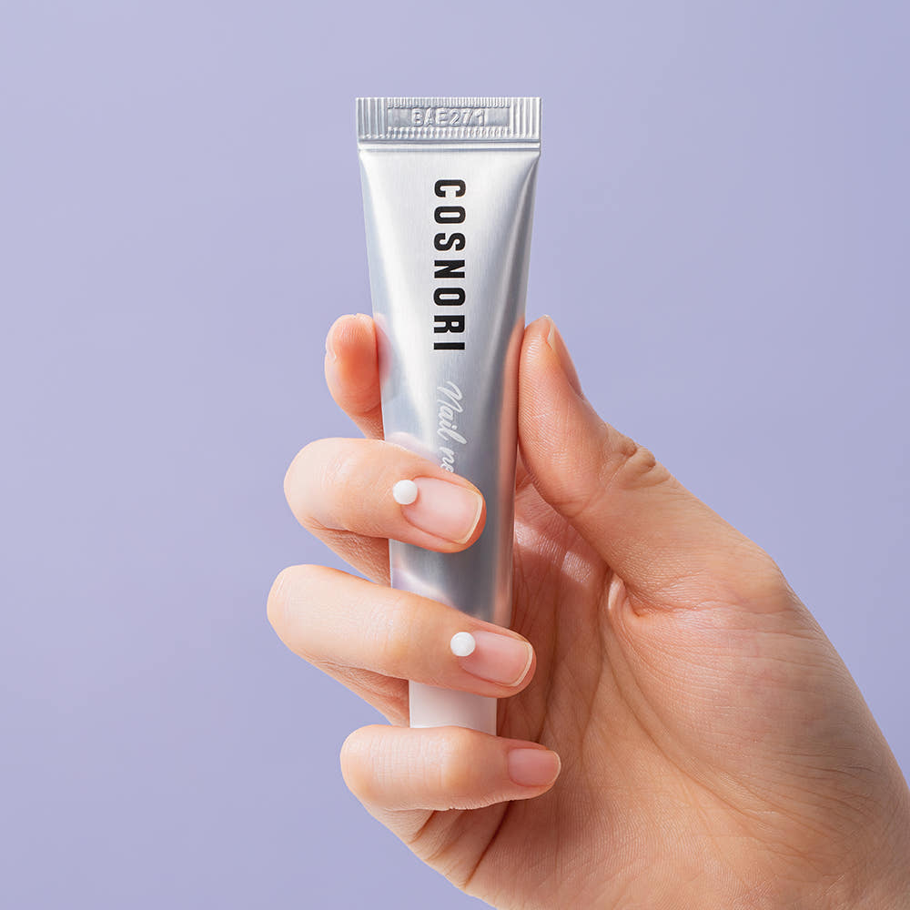 Main tenant COSNORI Nail Nutrition Silk Repair Nail Cream 15ml 2ea, crème de réparation des ongles sur fond clair.