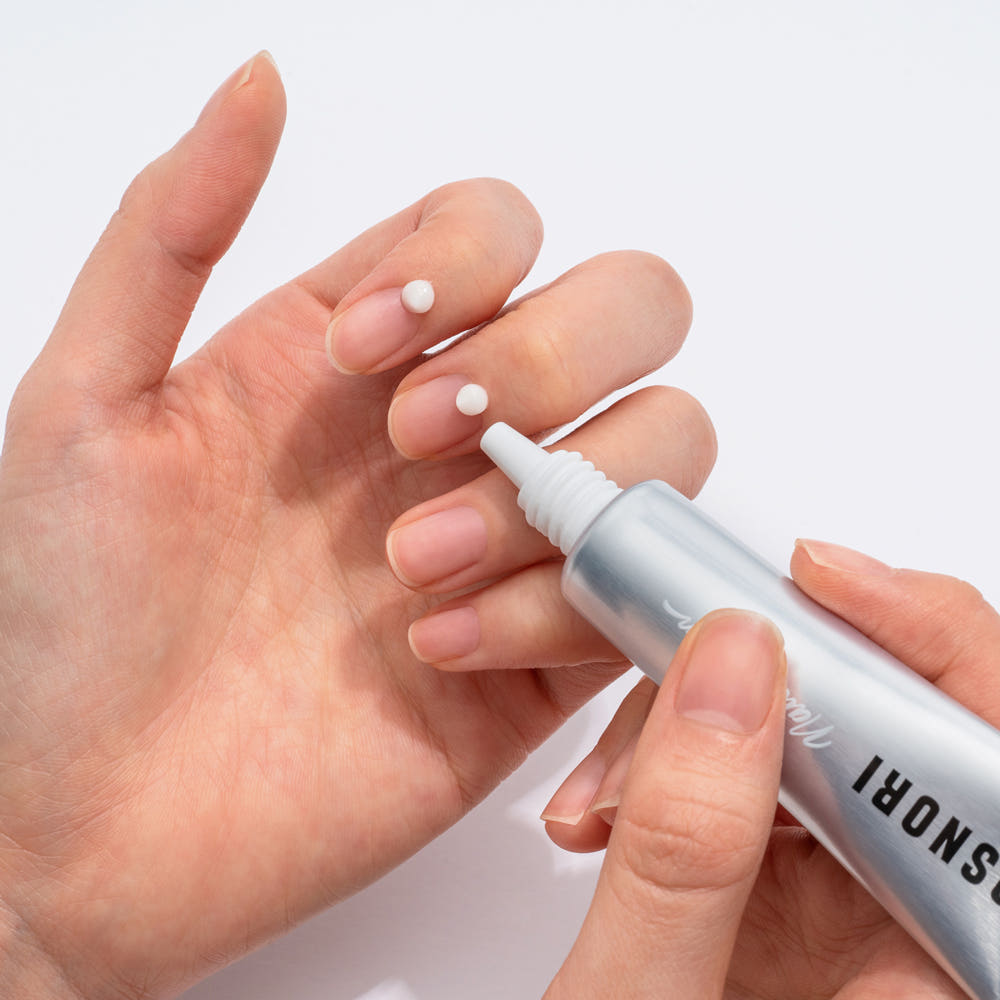 COSNORI Nail Nutrition Silk Repair Nail Cream 15ml 2ea, crème réparatrice sur ongles, main appliquant le produit, fond clair.