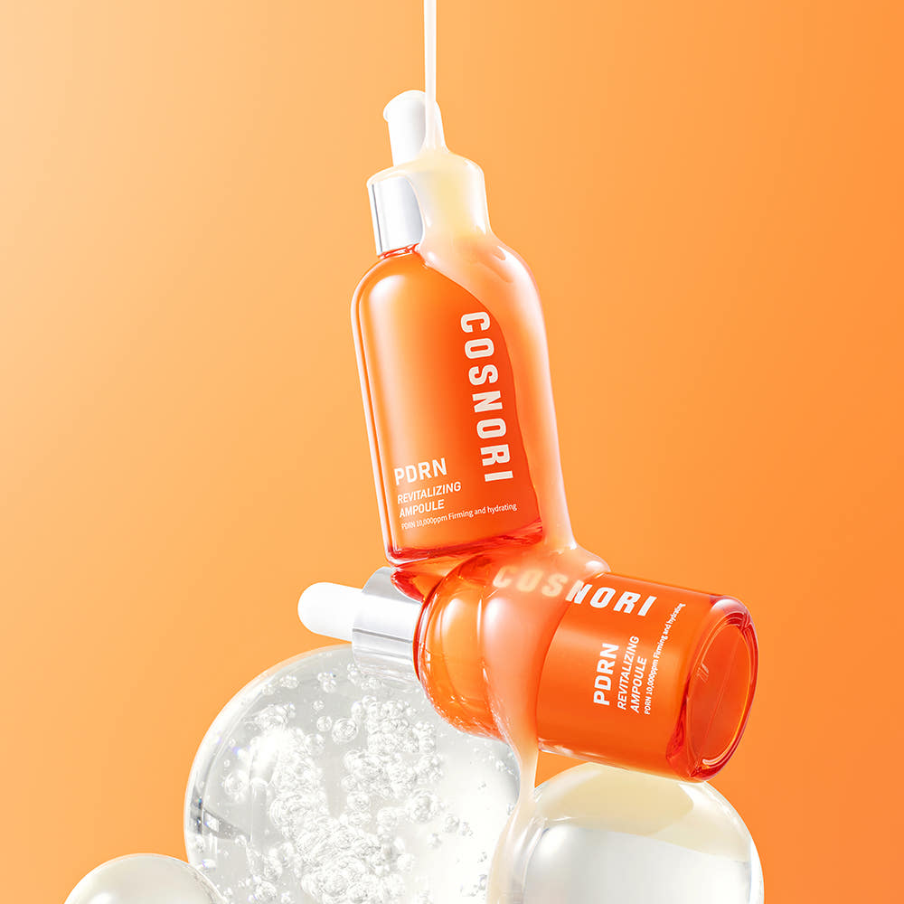 COSNORI PDRN Revitalizing Ampoule 50ml de COSNORI, flacons goutte sur fond orange, ambiance soins beauté