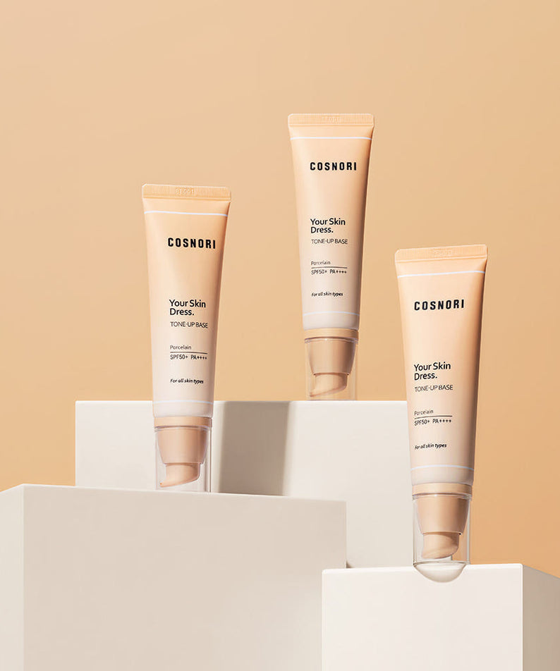 COSNORI Your Skin Dress Tone-Up Base 50ml de COSNORI, tubes cosmétiques sur socles blancs, fond beige.