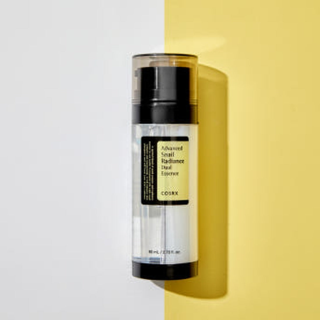 Décris l'image en français : COSRX Advanced Snail Radiance Dual Essence 80ml, bouteille COSRX sur fond jaune et blanc.
