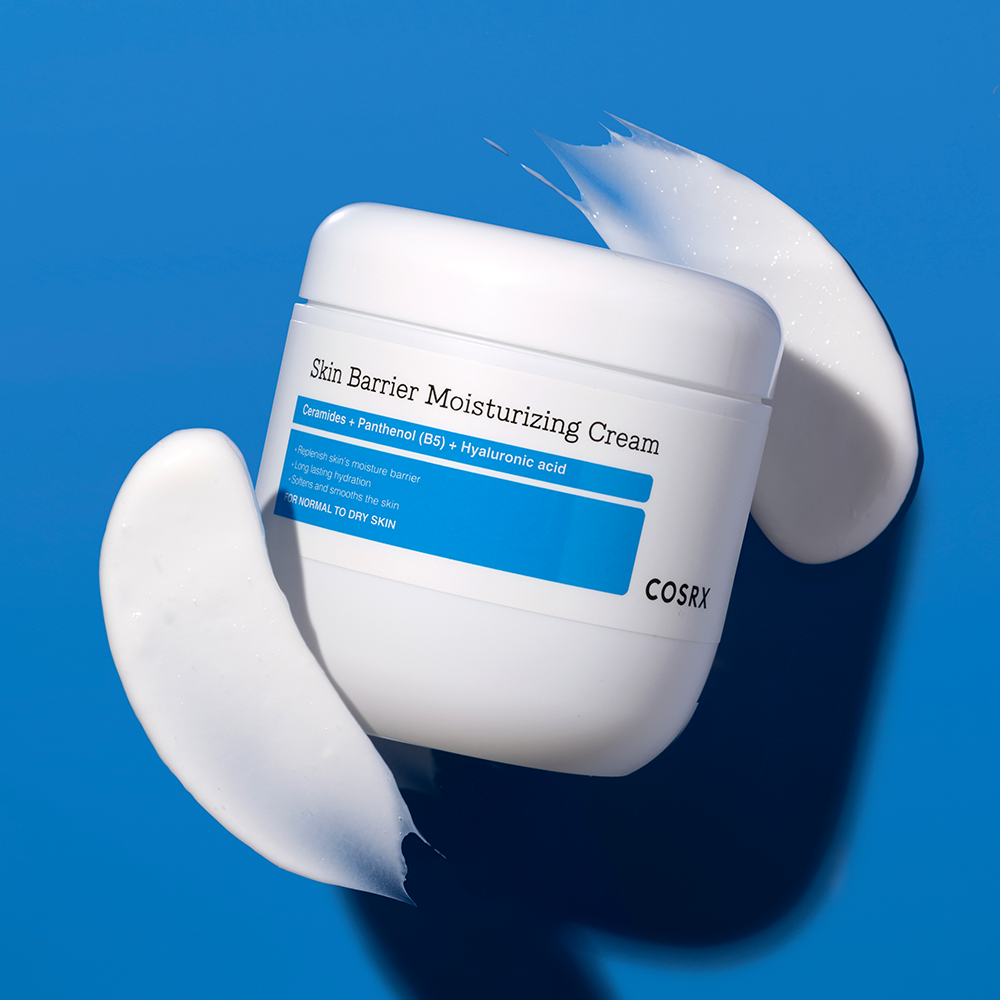 COSRX Skin Barrier Moisturizing Cream 450ml, pot de crème cosmétique blanc sur fond bleu, texture de crème en éclaboussures