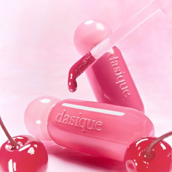 DASIQUE Dewy Glow Tint de la marque DASIQUE, flacon rose brillant sur fond pastel, gouttes et éclat déwy.