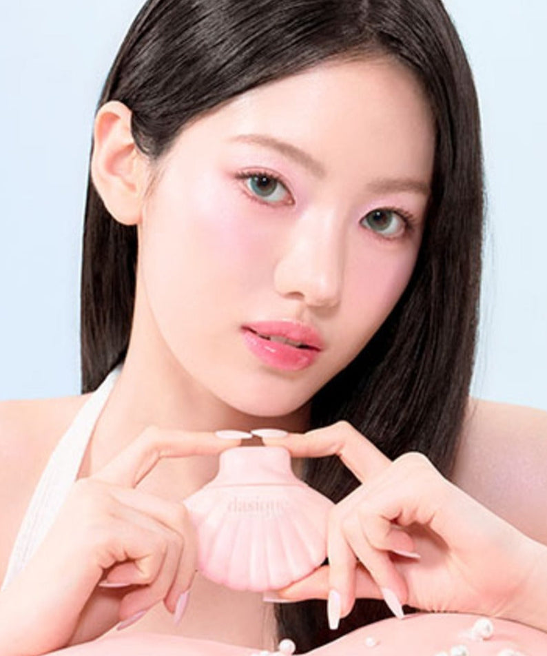 Jeune femme présentant le produit DASIQUE Glow Shell Base dans un emballage en forme de coquillage rose.