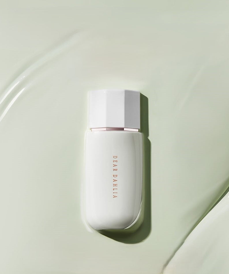 Flacon de DEAR DAHLIA Prime Layer Correcting Primer sur fond vert texturé.