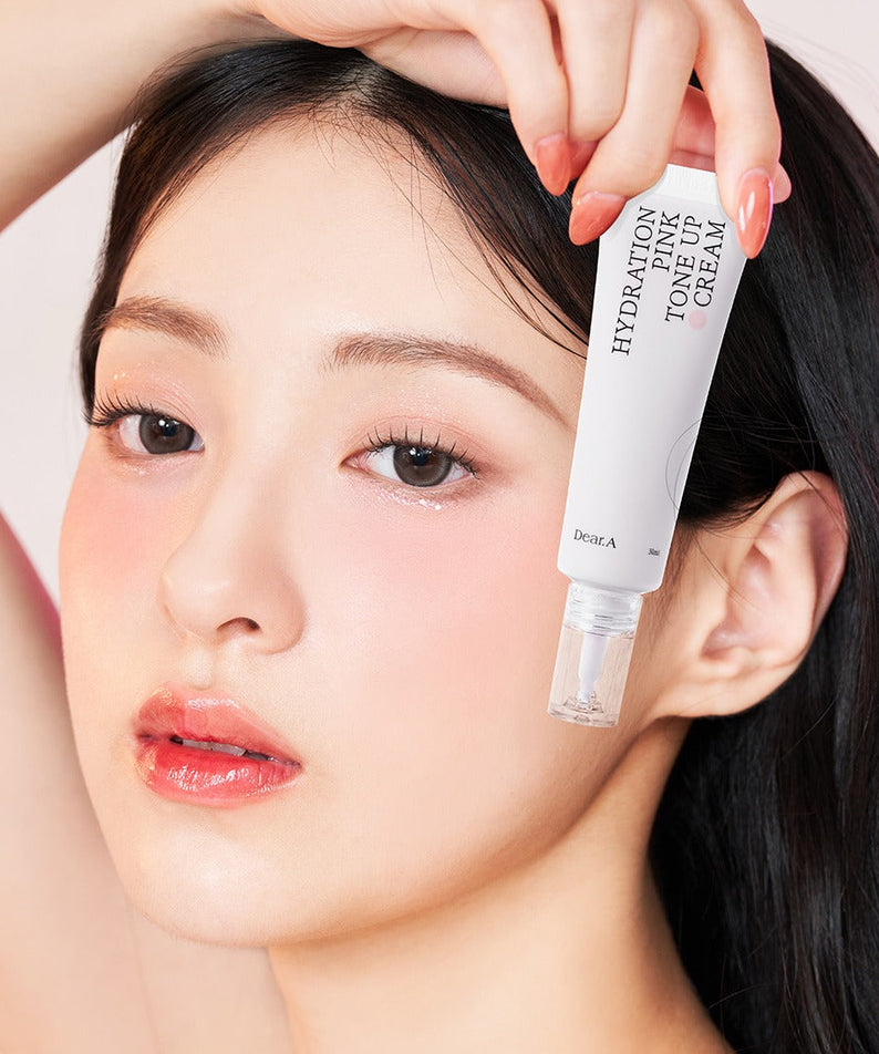 DEAR.A Hydration Pink Tone-Up Cream 30ml, la marque DEAR.A en tube rose, pose maquillage avec main sur visage, contexte beauté.
