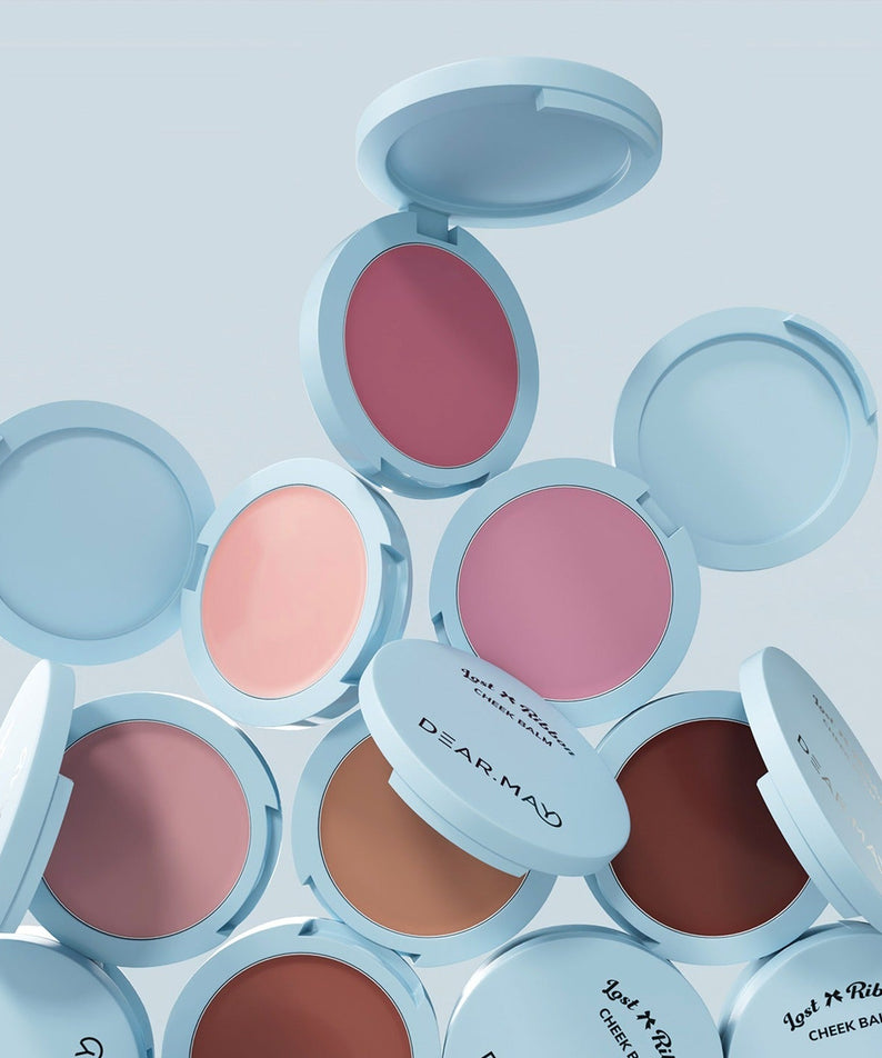 Collection de baumes DEAR MAY Lost Ribbon Check Balm dans des teintes variées. Cosmétiques élégants dans des boîtes ouvertes bleues pastel.