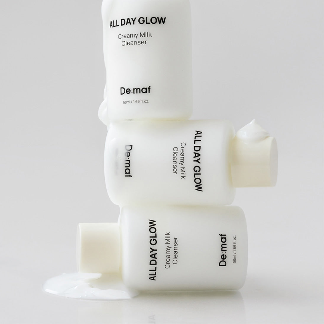 DE:MAF All Day Glow Creamy Milk Cleanser 50ml de De-Maf, flacons crème et lait nettoyant sur fond clair.