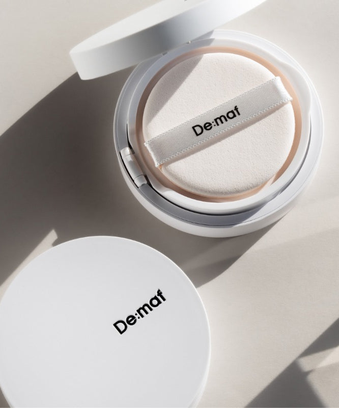 DE:MAF Bora Blossom Tone-Up Cushion De:maf en coussin tonifiant, packaging ouvert, lumière naturelle sur fond clair.
