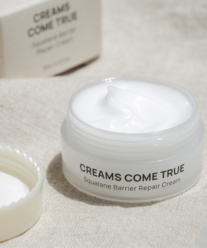 DE:MAF Creamscumtrue Squalane Barrier Repair Cream 15ml, crème blanche dans pot, sur tissu beige, marque visible.