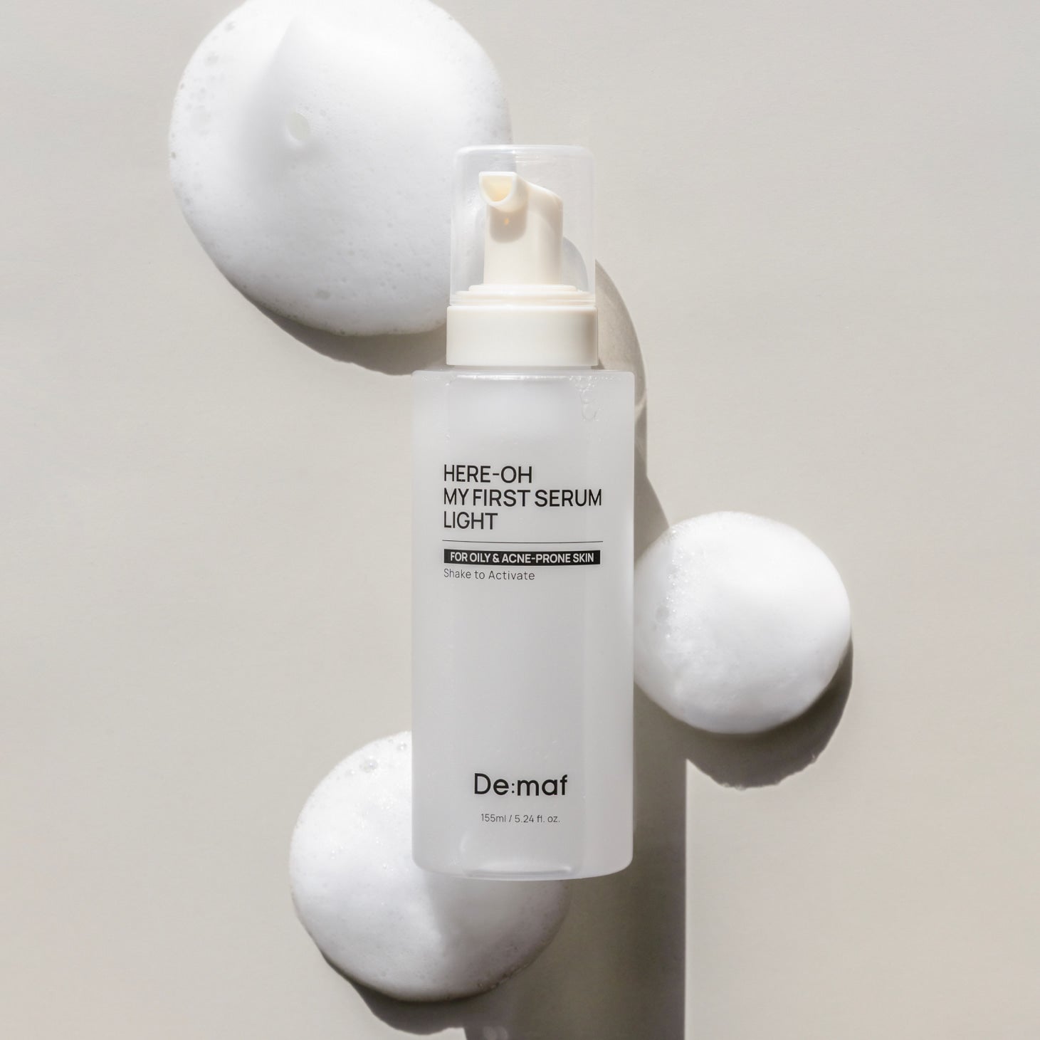 DE:MAF Here-Oh My First Serum Light 155ml de De:maf, flacon sur fond crème avec sphères décoratives, contexte skincare