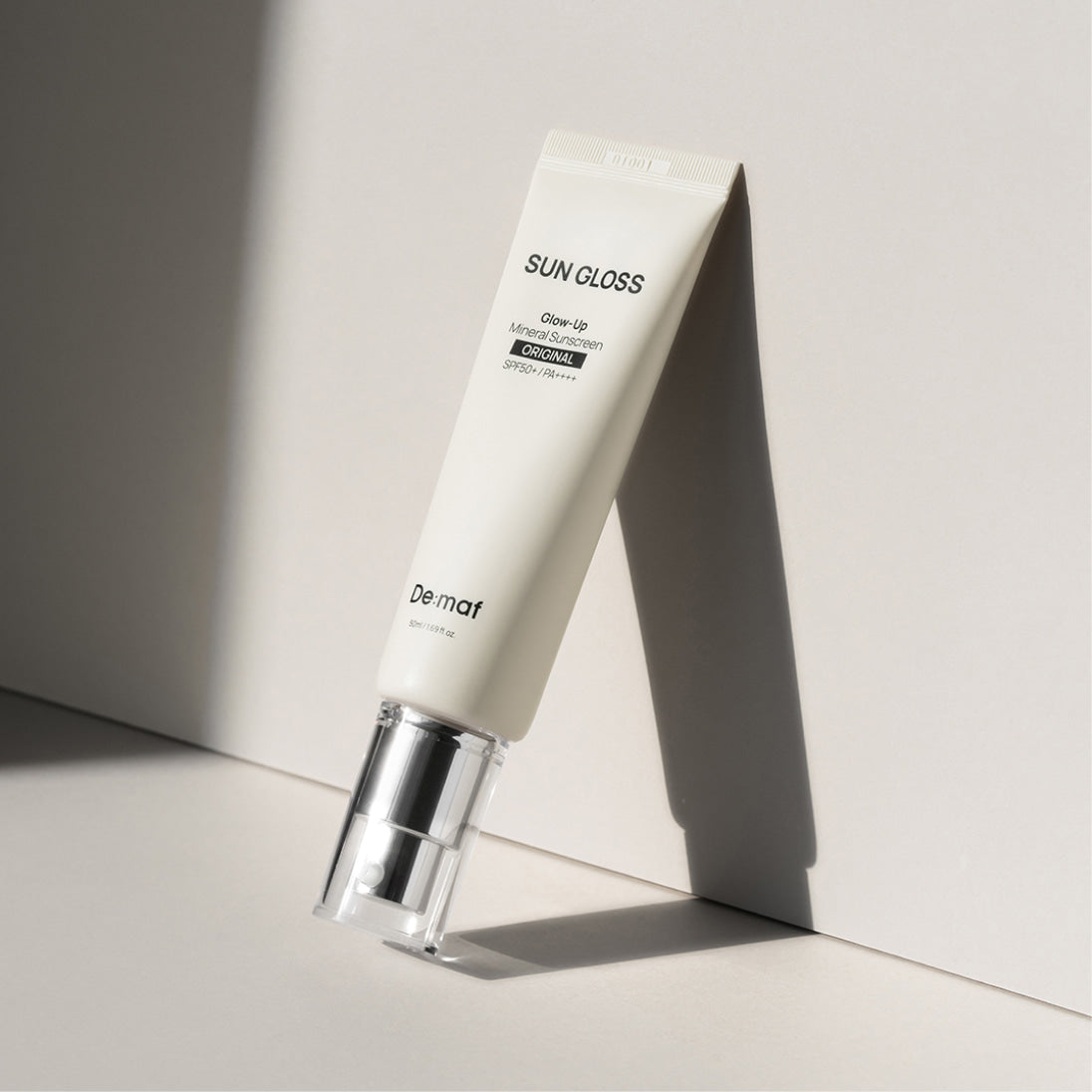 DE:MAF Sun Gloss Glow Up Inorganic Sunscreen 50ml Original, tube crème SPF DeMaf sur fond clair, éclairage studio.
