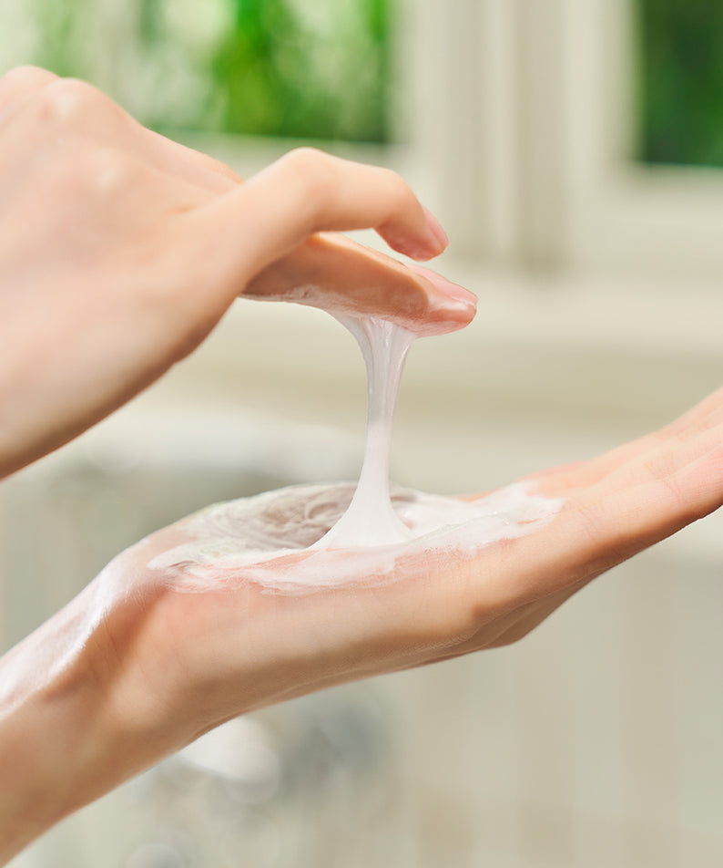 Application du DEWYTREE Hi Amino All Enzyme Powder Wash 50g sur la main, montrant une texture crémeuse et moussante dans une salle de bain lumineuse.