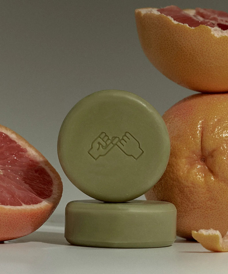 DONGGUBAT Correct Shampoo Bar For Dry Skin, savon solide présenté sur fond neutre, agrumes en arrière-plan.