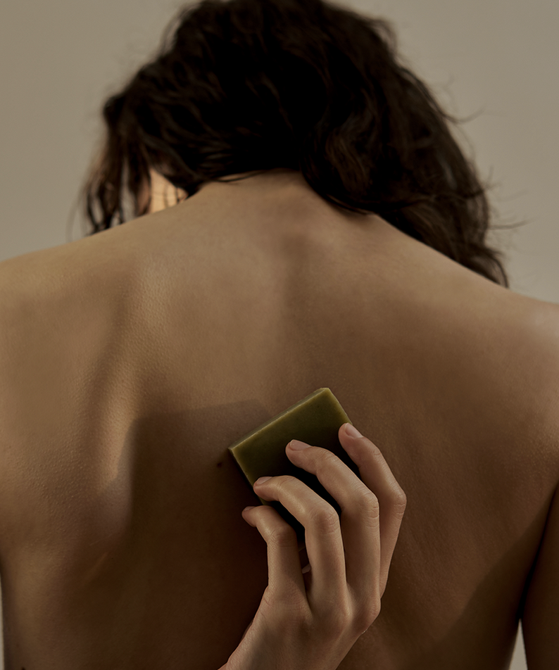Décris l'image en français : DONGGUBAT Dream Soap Lattuce, marque DONGGUBAT, tenue nue dos, savon vert sur la peau.