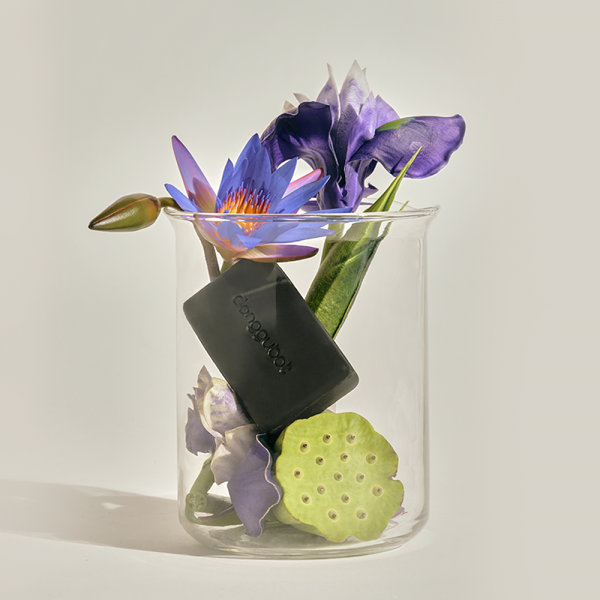 DONGGUBAT Field Blooming Perfume Shampoo Bar Calming 80g, barrette noire dans bocal avec fleurs violettes, contexte visuel