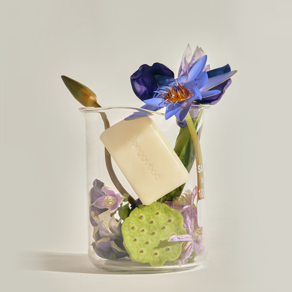 Décris l'image en français : DONGGUBAT Field Blooming Perfume Shampoo Bar Volume 80g, barrette blanche, fleurs bleues sur fond clair.